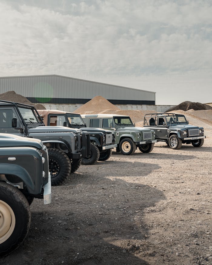 Row of classic off-road vehicles parked in a barren industrial landscape under a cloudy sky.
